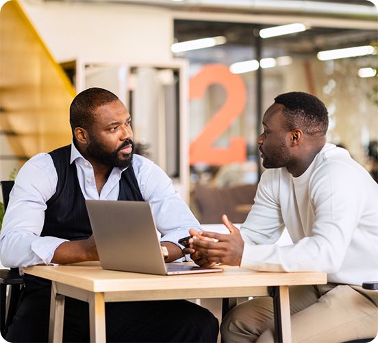 Two business professionals talking across a table with a laptop
